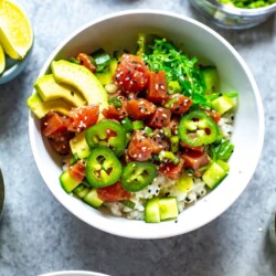 A close-up of an ahi tuna poke bowl topped with avocado slices, jalapeno slices, and sesame seeds.