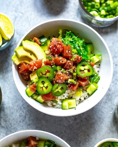 A close-up of an ahi tuna poke bowl topped with avocado slices, jalapeno slices, and sesame seeds.