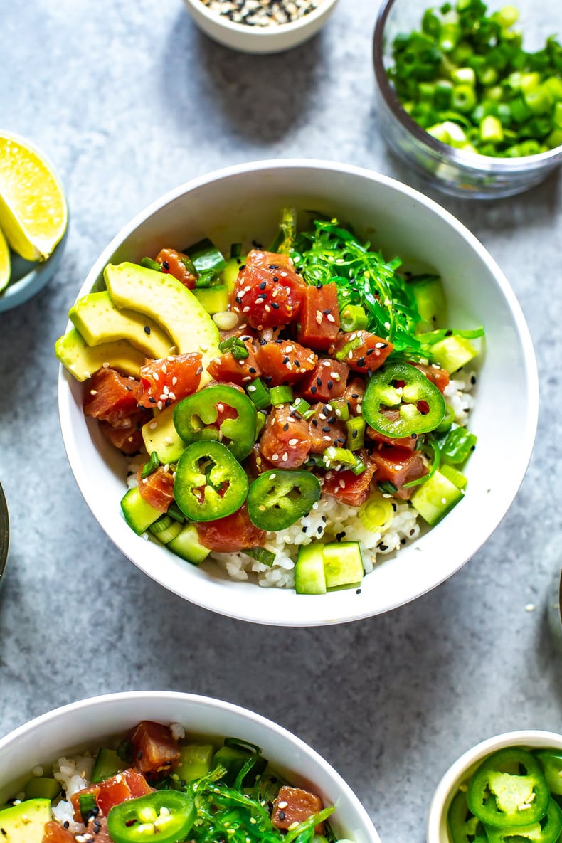 A close-up of an ahi tuna poke bowl topped with avocado slices, jalapeno slices, and sesame seeds.