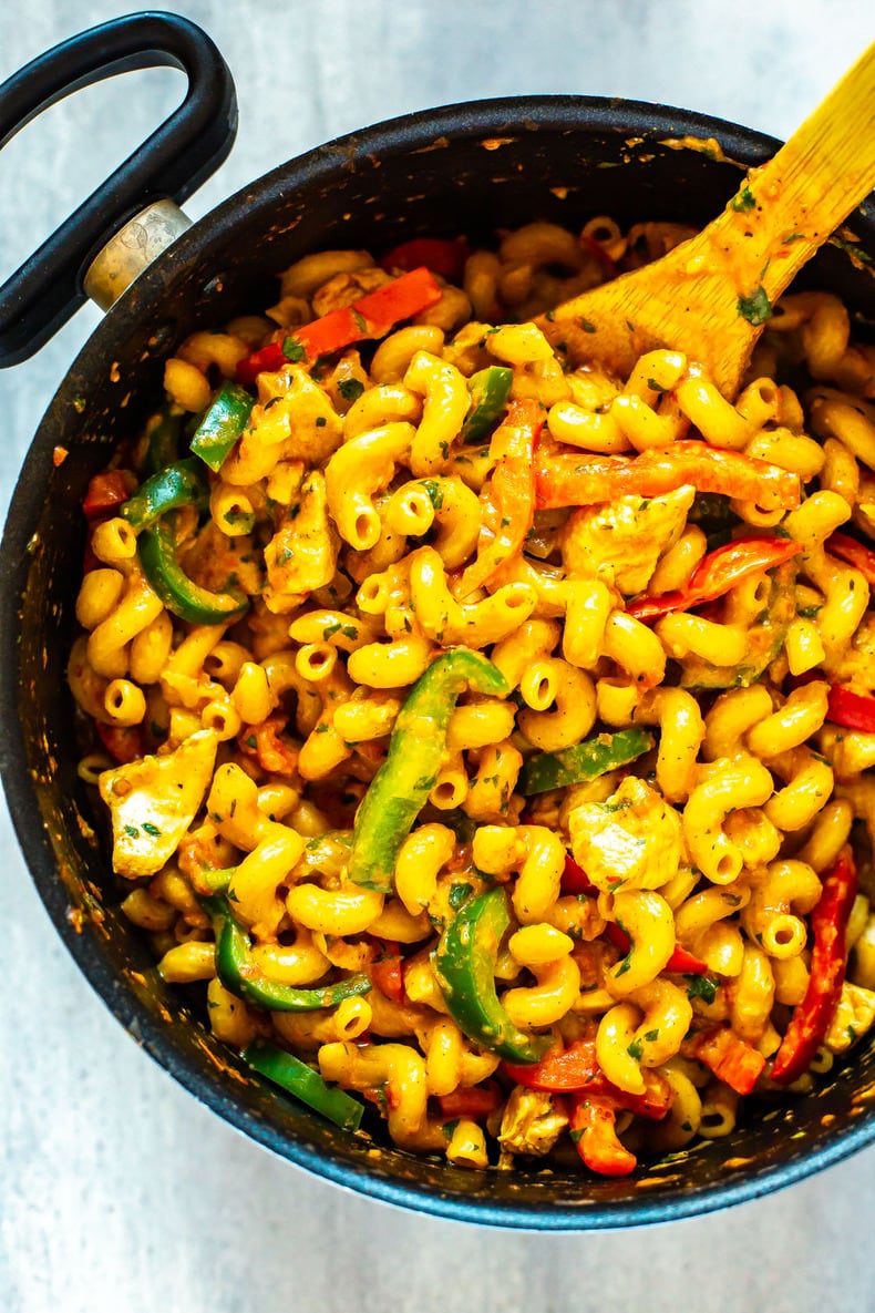 A big pot of cajun chicken pasta with a wooden spoon inside.