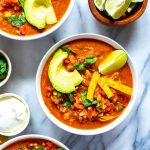 Three bowls of Instant Pot chicken enchilada soup with sour cream and cilantro on the side.