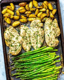 A sheet pan with roasted potatoes, seasoned chicken breasts, and asparagus on top.