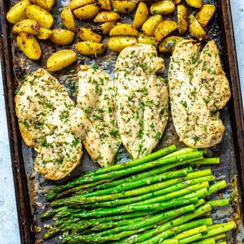 A sheet pan with roasted potatoes, seasoned chicken breasts, and asparagus on top.