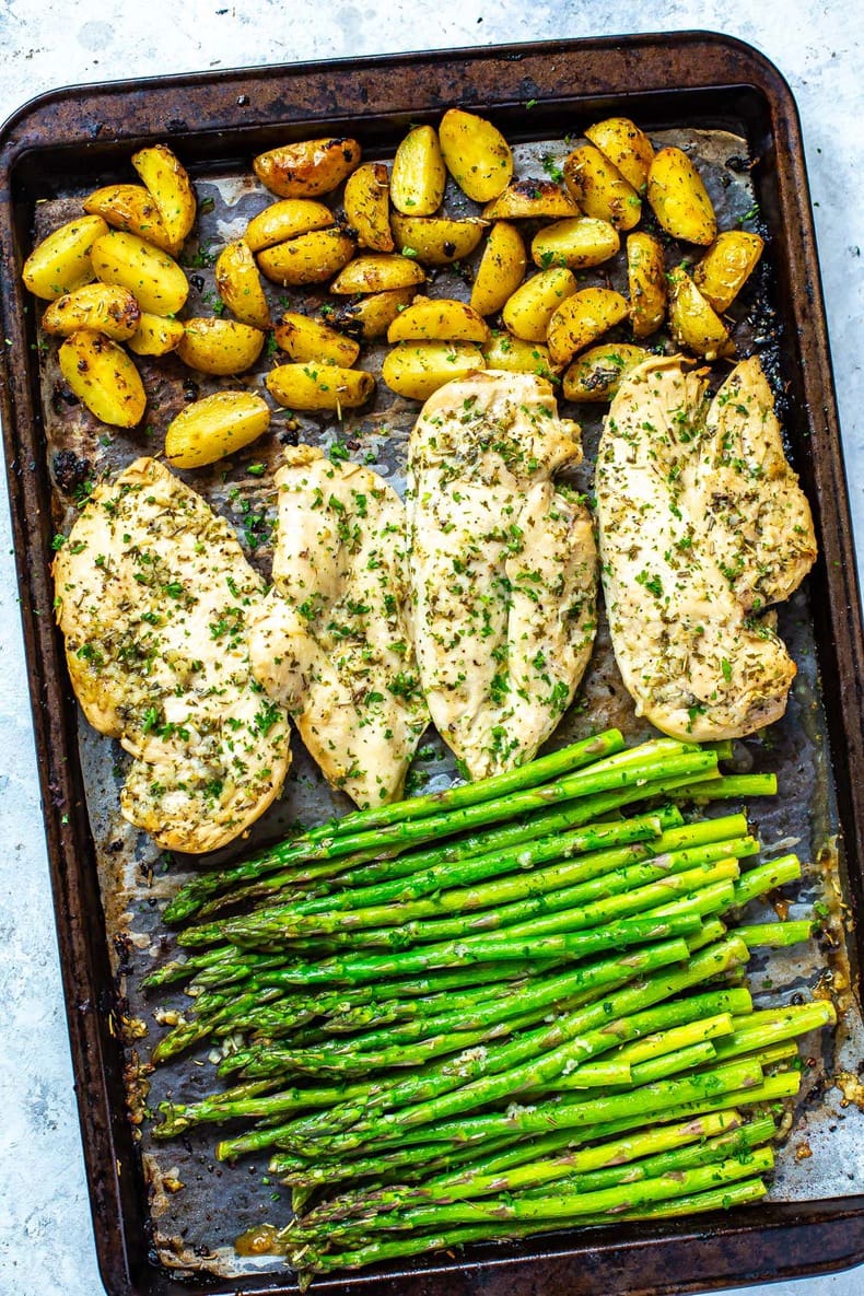 A sheet pan with roasted potatoes, seasoned chicken breasts, and asparagus on top.