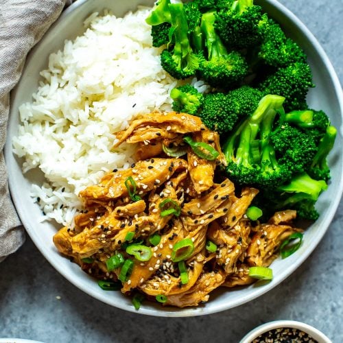 One bowl filled with white rice, chicken teriyaki and steamed broccoli garnished with sesame seeds and green onions.