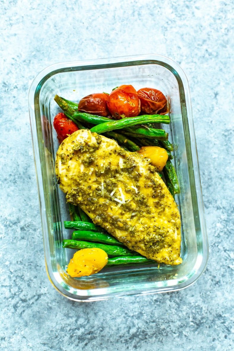 chicken with pesto sauce and cooked vegetables in glass meal prep container