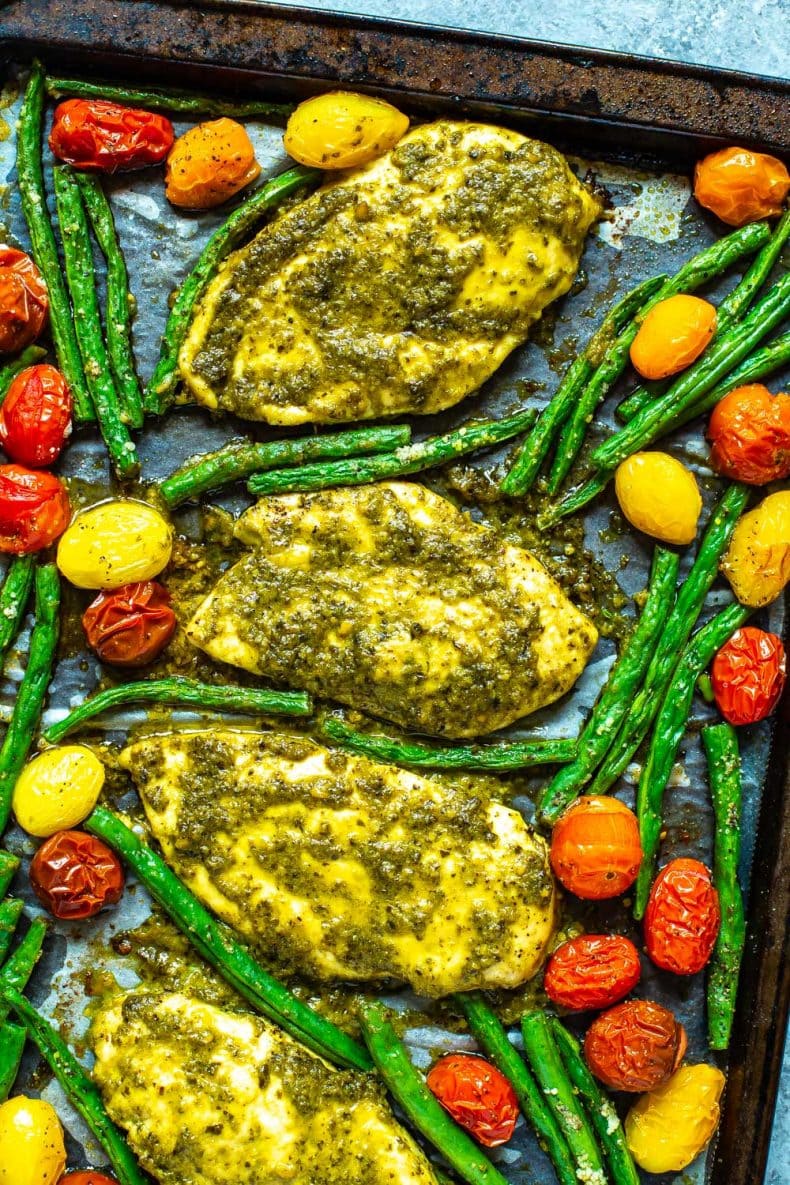 oven baked pesto chicken on baking sheet with roasted tomatoes and asparagus