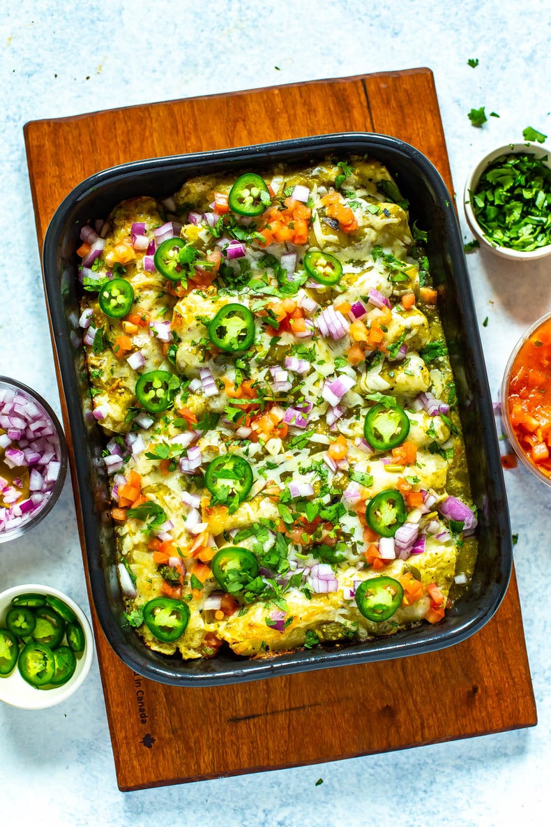 Chicken enchiladas verdes in a black casserole dish garnished with sliced jalapeno, diced red onion, and cilantro.