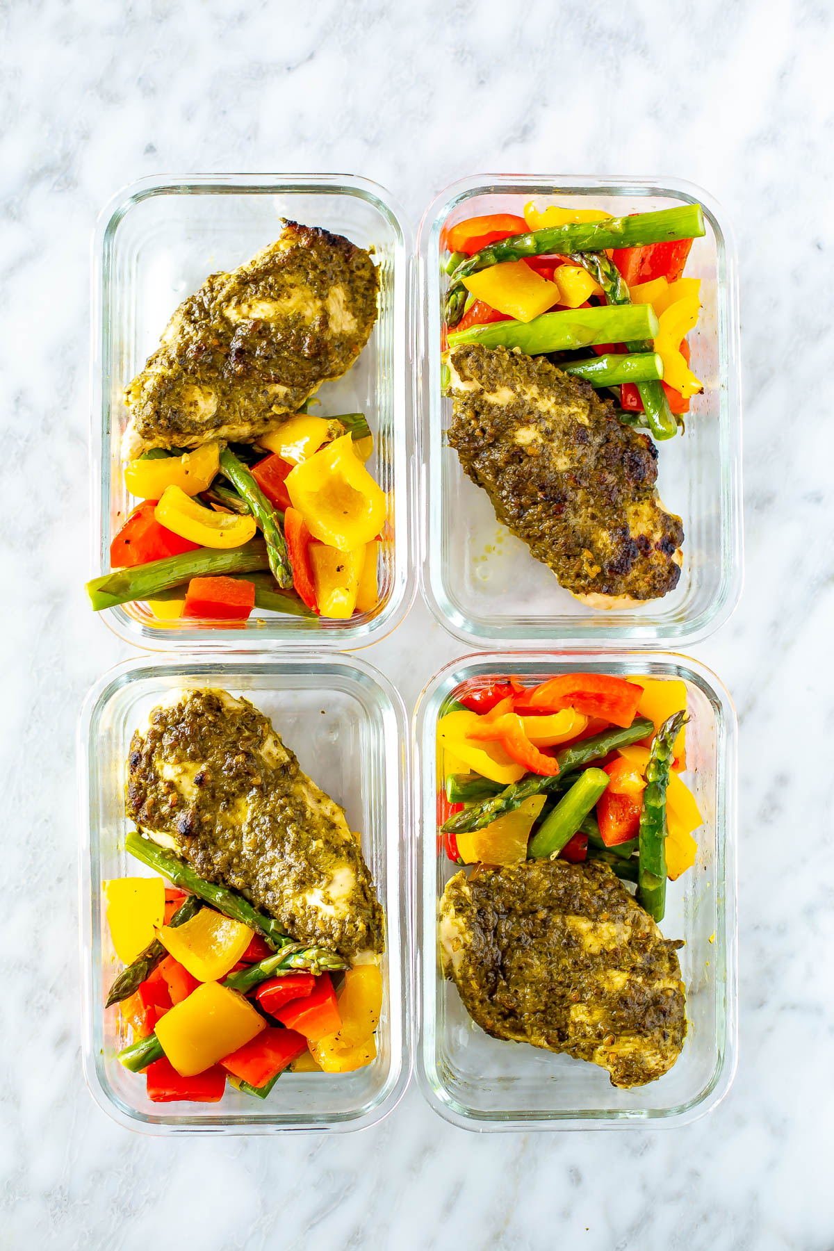 Pesto coated chicken cutlets with asparagus, red pepper and yellow pepper in square glass meal prep containers.