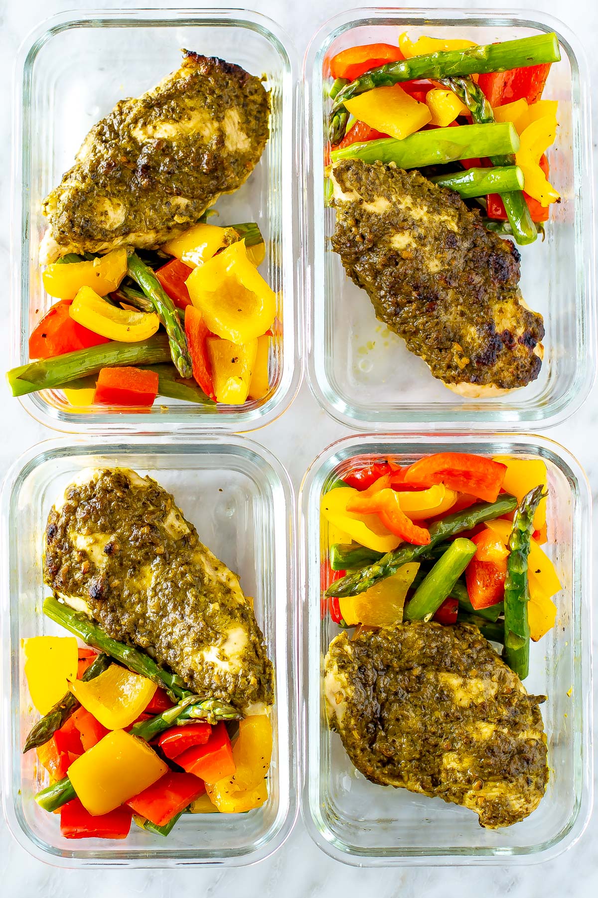 Pesto coated chicken cutlets with asparagus, red pepper and yellow pepper in square glass meal prep containers, zoomed in.
