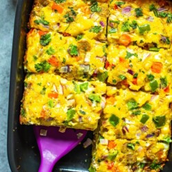 A cooked sausage hashbrown breakfast casserole in a black casserole dish cut into 8 pieces with a spatula picking up a piece.