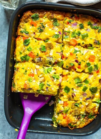 A cooked sausage hashbrown breakfast casserole in a black casserole dish cut into 8 pieces with a spatula picking up a piece.