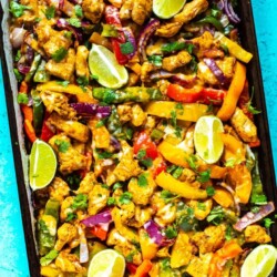 A sheet pan with chicken fajitas topped with lime slices and garnished with cilantro.