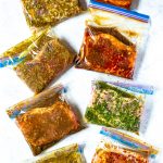 8 different freezer bags, each containing a different kind of marinated steak.