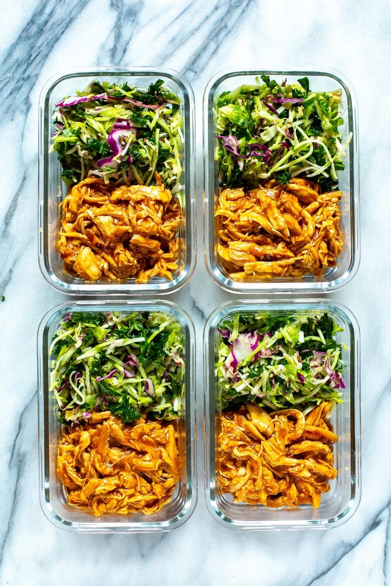 Four meal prep containers, each containing shredded crockpot BBQ chicken and kale slaw.