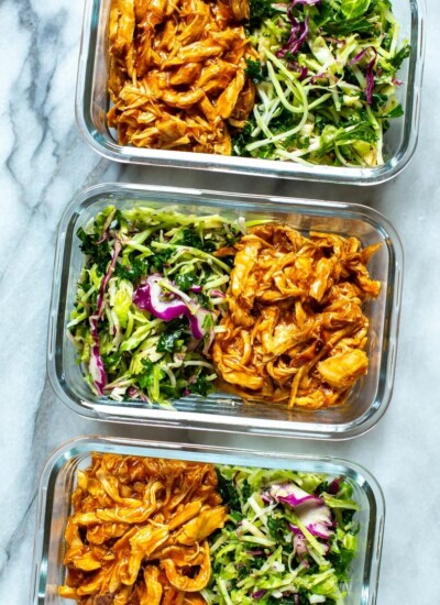 Three meal prep containers, each containing shredded crockpot BBQ chicken and kale slaw.