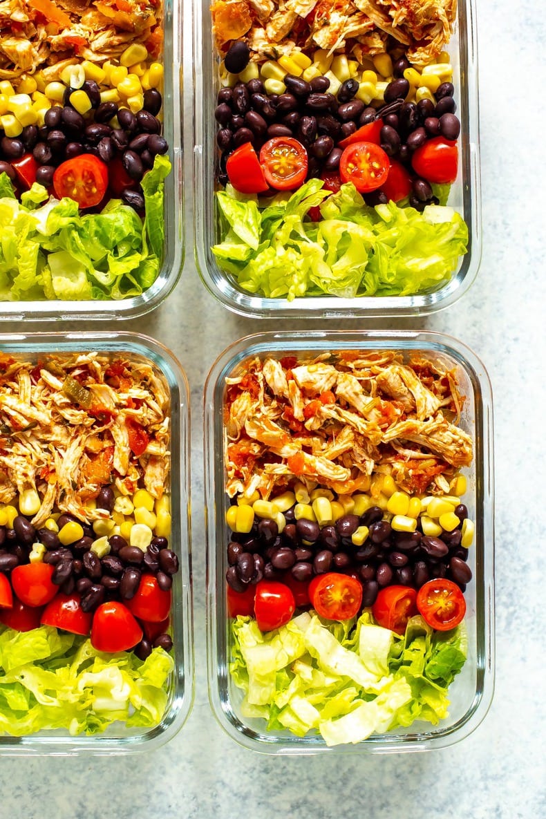 Four meal prep containers, each containing crockpot salsa chicken, corn, black beans, cherry tomatoes and lettuce.
