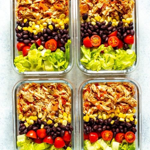 Four meal prep containers, each containing crockpot salsa chicken, corn, black beans, cherry tomatoes and lettuce.