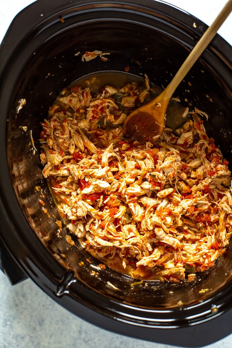 A slow cooker filled with crockpot salsa chicken with a spoon inside.