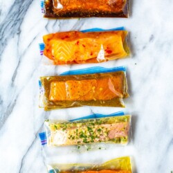 Five freezer bags with marinated salmon filets in five different marinades: Teriyaki, Chili Lime, Maple Dijon, Lemon Garlic and Plain.