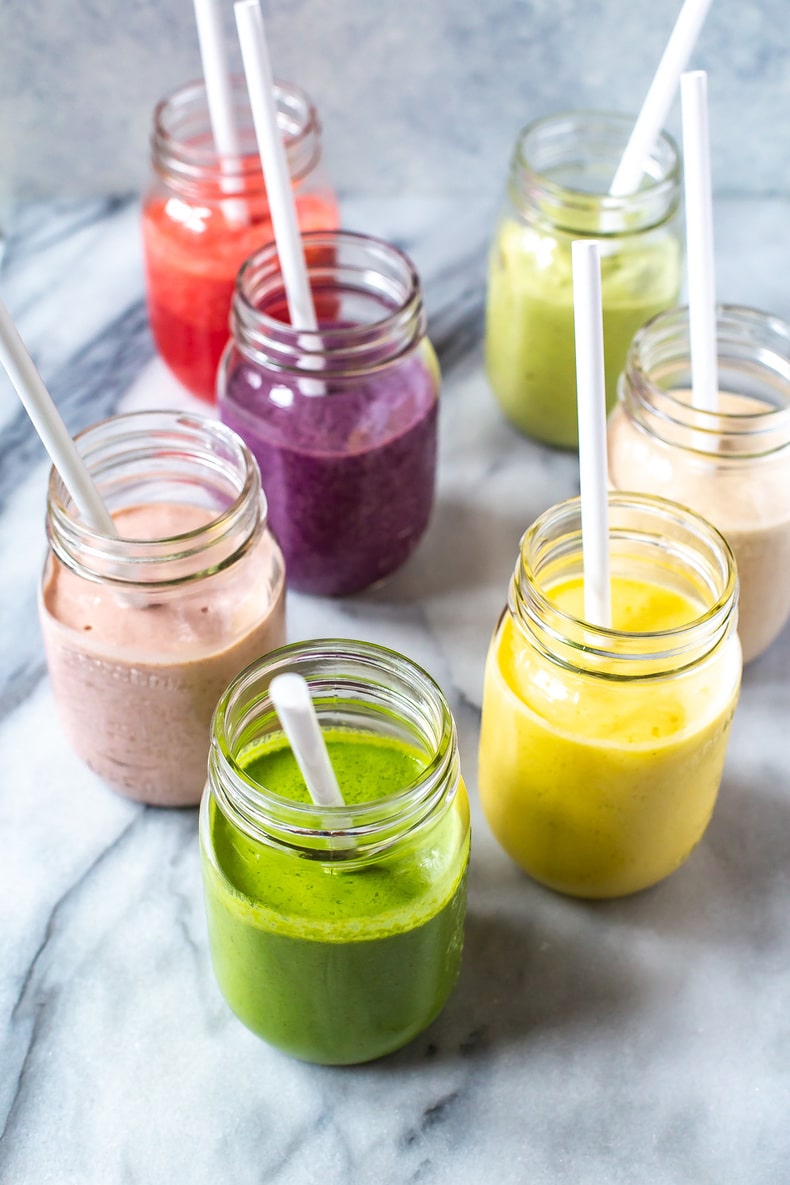 7 mason jars, each filled with a different smoothie.