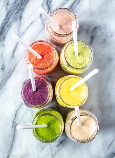 An overhead shot of 7 mason jars, each filled with a different smoothie.