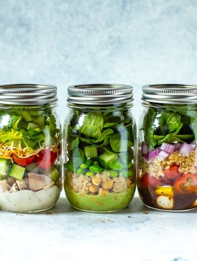 5 mason jars in a row, each containing a different salad inside.