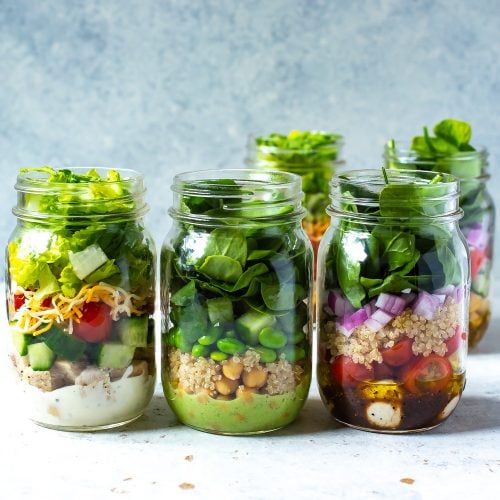 3 mason jars in a row, each containing a different salad inside.