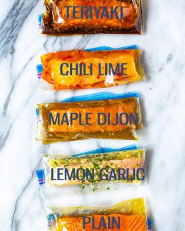 Five freezer bags with marinated salmon filets, labelled "Teriyaki", "Chili Lime", "Maple Dijon", "Lemon Garlic" and "Plain".