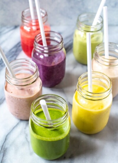 7 mason jars, each filled with a different smoothie.