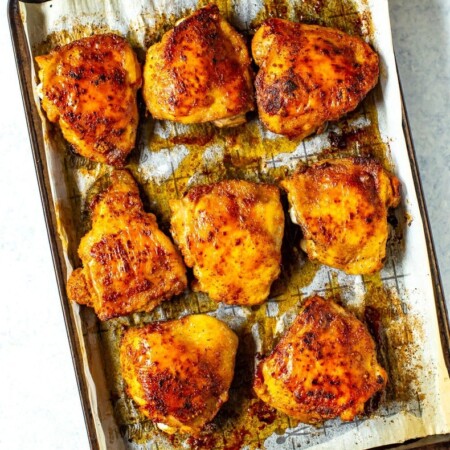 Baked seasoned chicken thighs on a sheet pan prepared with parchment paper.