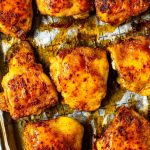 A close-up of seasoned baked chicken thighs on a sheet pan with prepared with parchment paper.