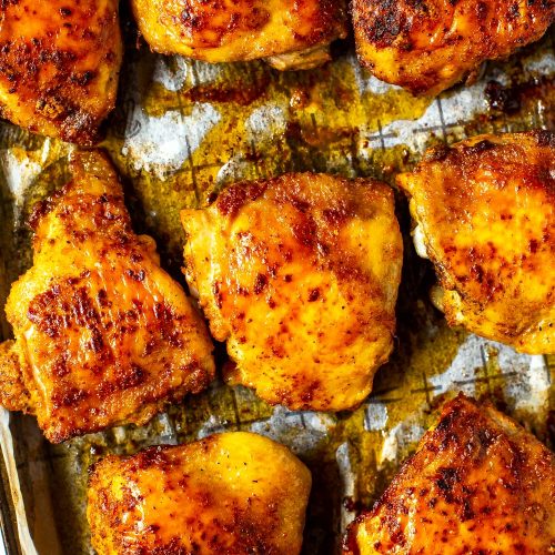 A close-up of seasoned baked chicken thighs on a sheet pan with prepared with parchment paper.