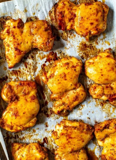 A close-up of seasoned baked chicken thighs on a sheet pan with prepared with parchment paper.