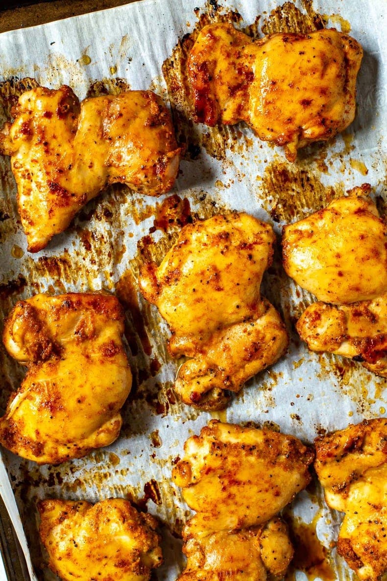 A close-up of seasoned baked chicken thighs on a sheet pan with prepared with parchment paper.