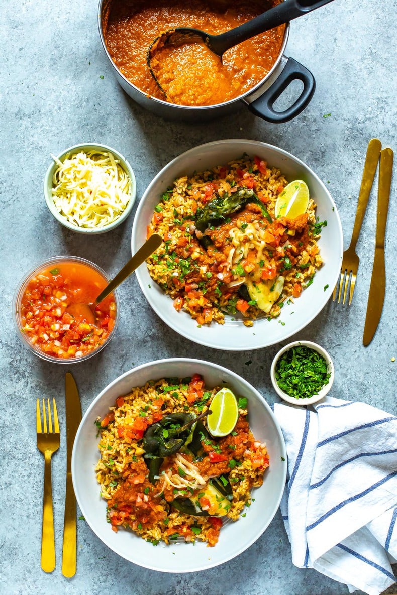 Skinny Chile Rellenos with melted cheese plated over Mexican rice with pico de gallo overtop. Bowls of cilantro, pico de gallo, cheese and red sauce on the side.