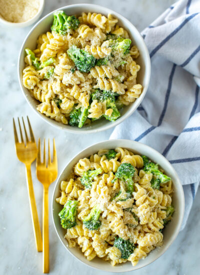 Two bowls of broccoli alfredo pasta with cutlery next to them.