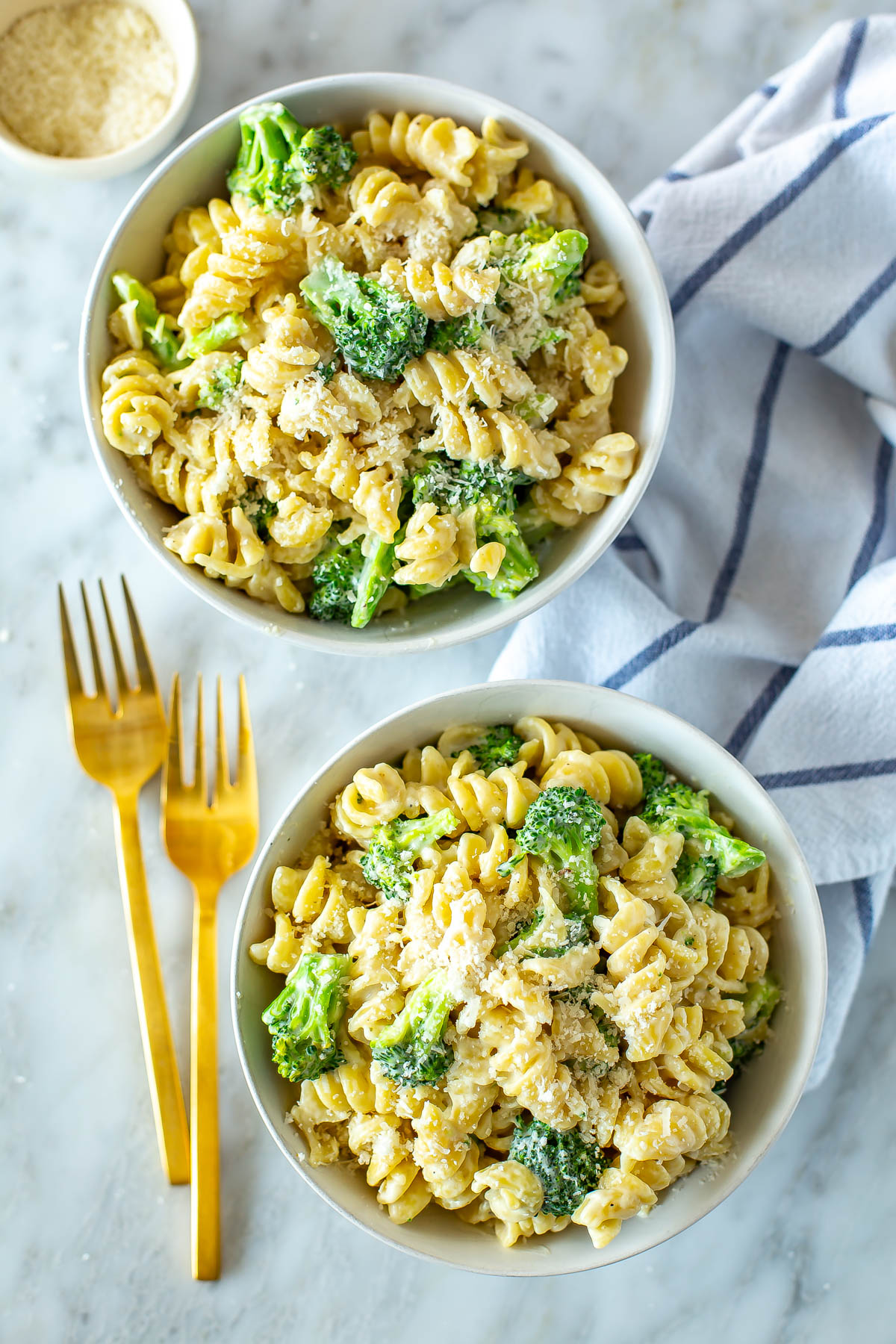 Two bowls of broccoli alfredo pasta with cutlery next to them.