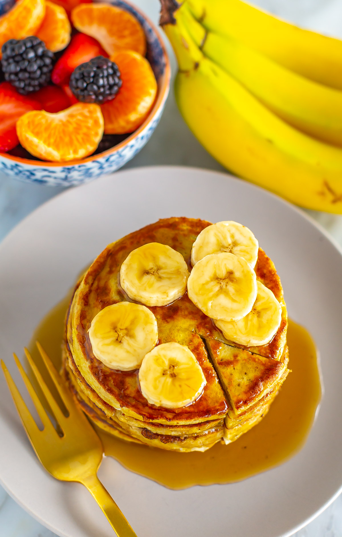 An overhead shot of banana egg pancakes with a bowl of fruit next to it. 