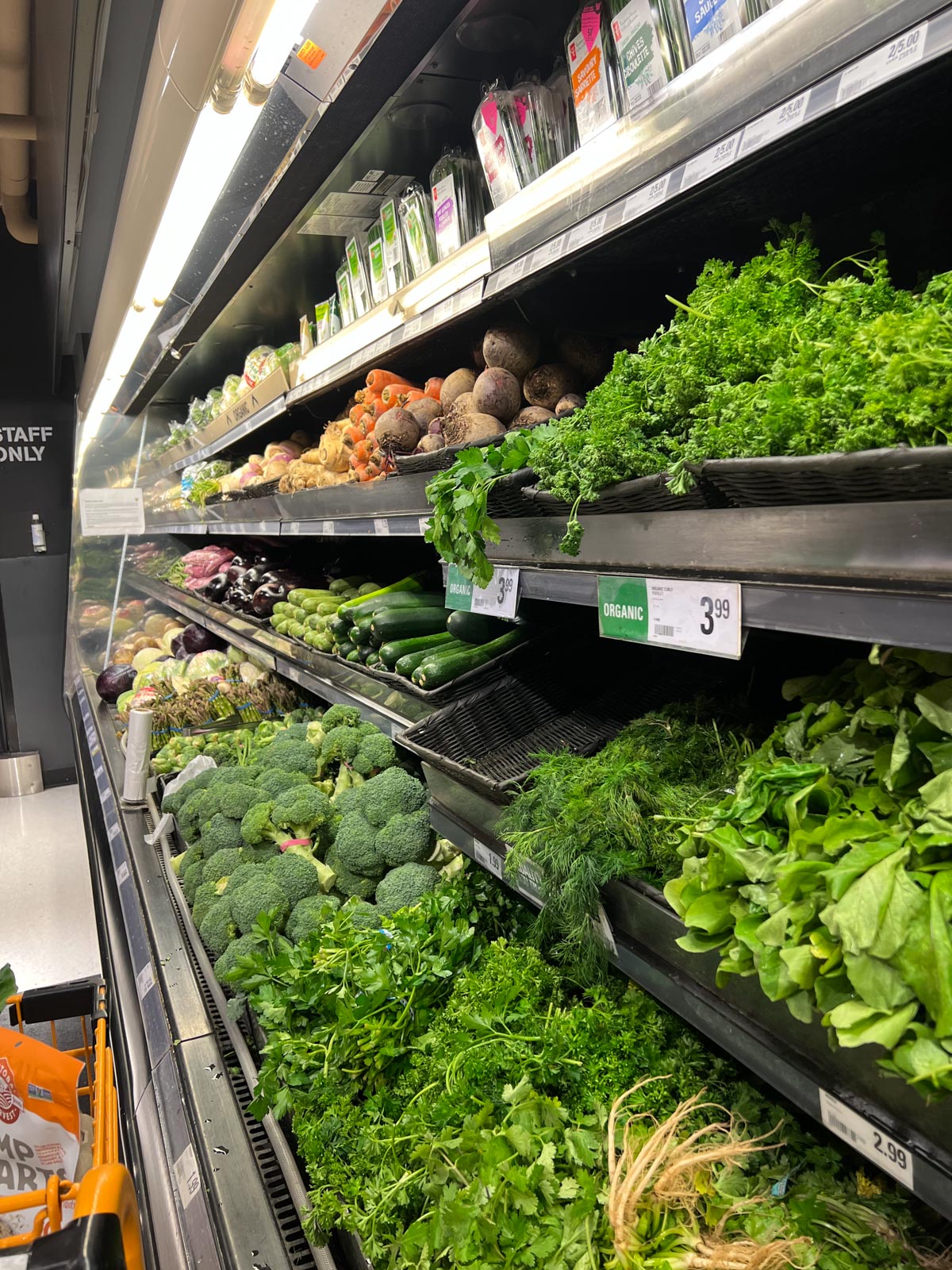 The produce aisle of the grocery store with greens, herbs and broccoli visible.