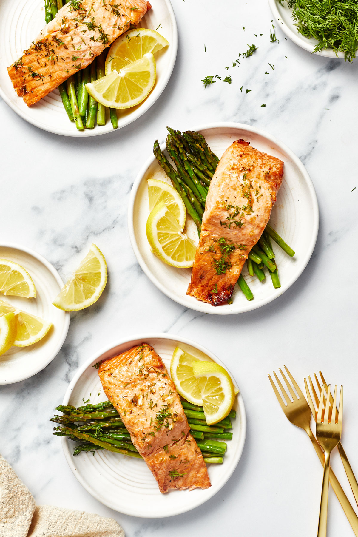 A zoomed-out shot with three plates, each with a bed of asparagus topped with air fryer salmon, garnished with lemon slices.