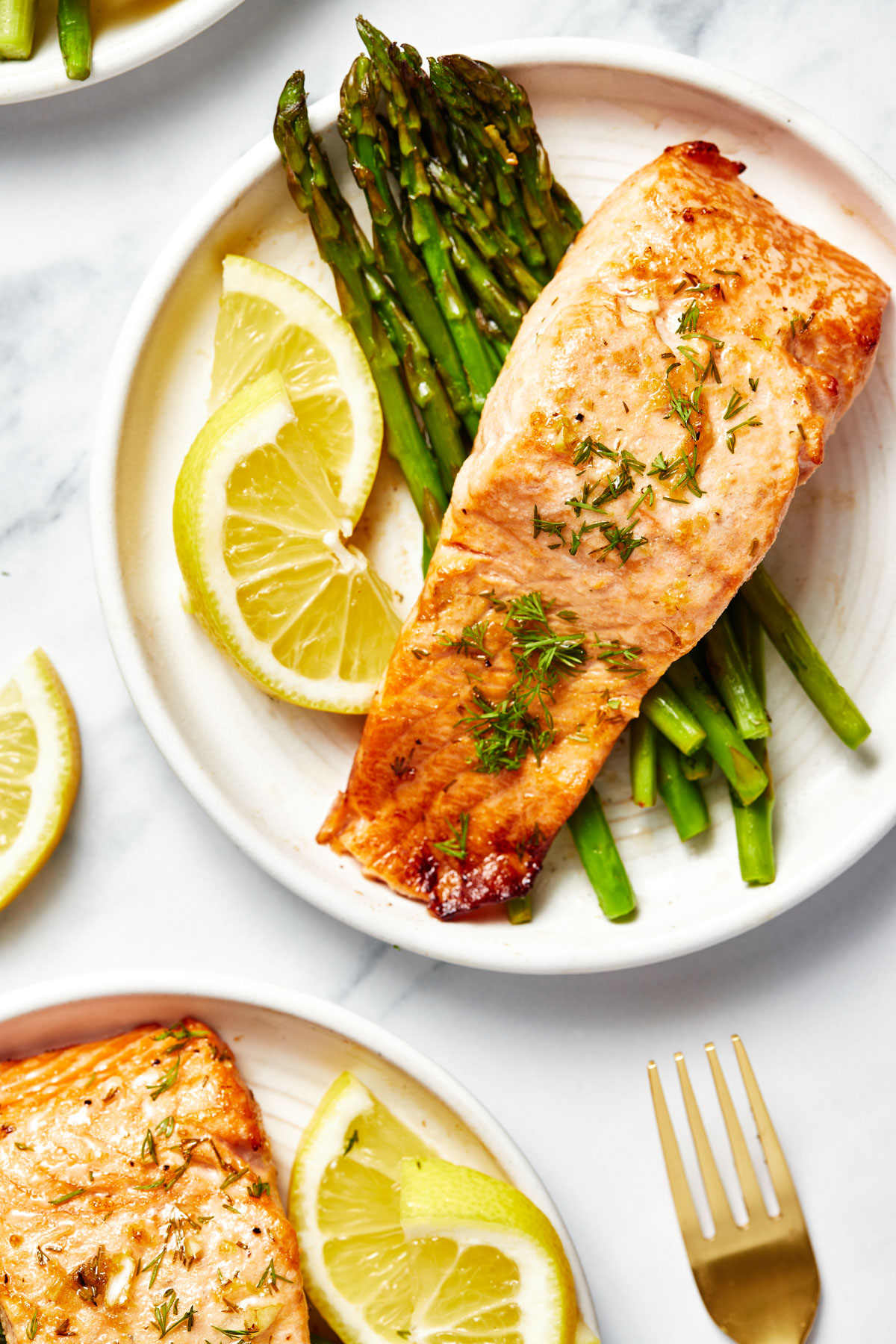 A close-up of two plates, each with a bed of asparagus topped with air fryer salmon, garnished with lemon slices.