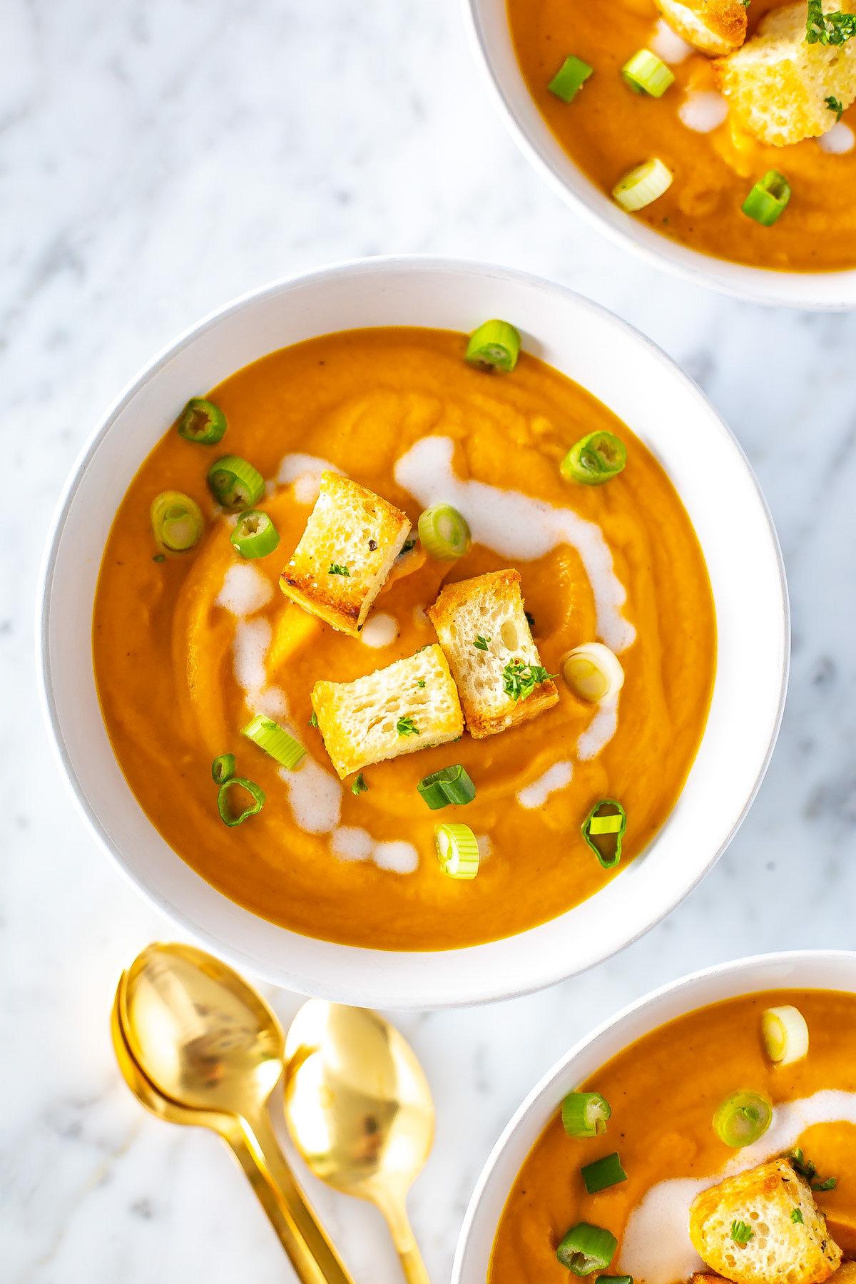 A close-up of a bowl of creamy coconut carrot soup topped with croutons.