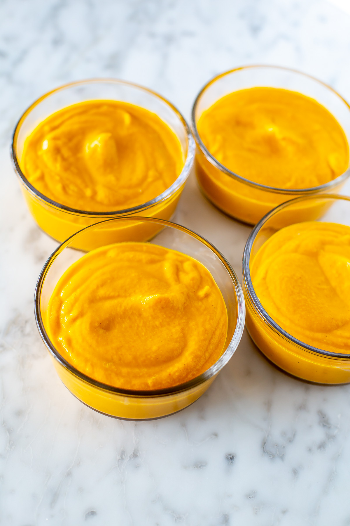 Four round glass meal prep containers, each filled with creamy coconut carrot ginger soup.