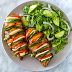 A plate with hasselback caprese chicken with a side salad.