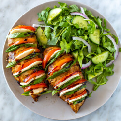 A plate with hasselback caprese chicken with a side salad.