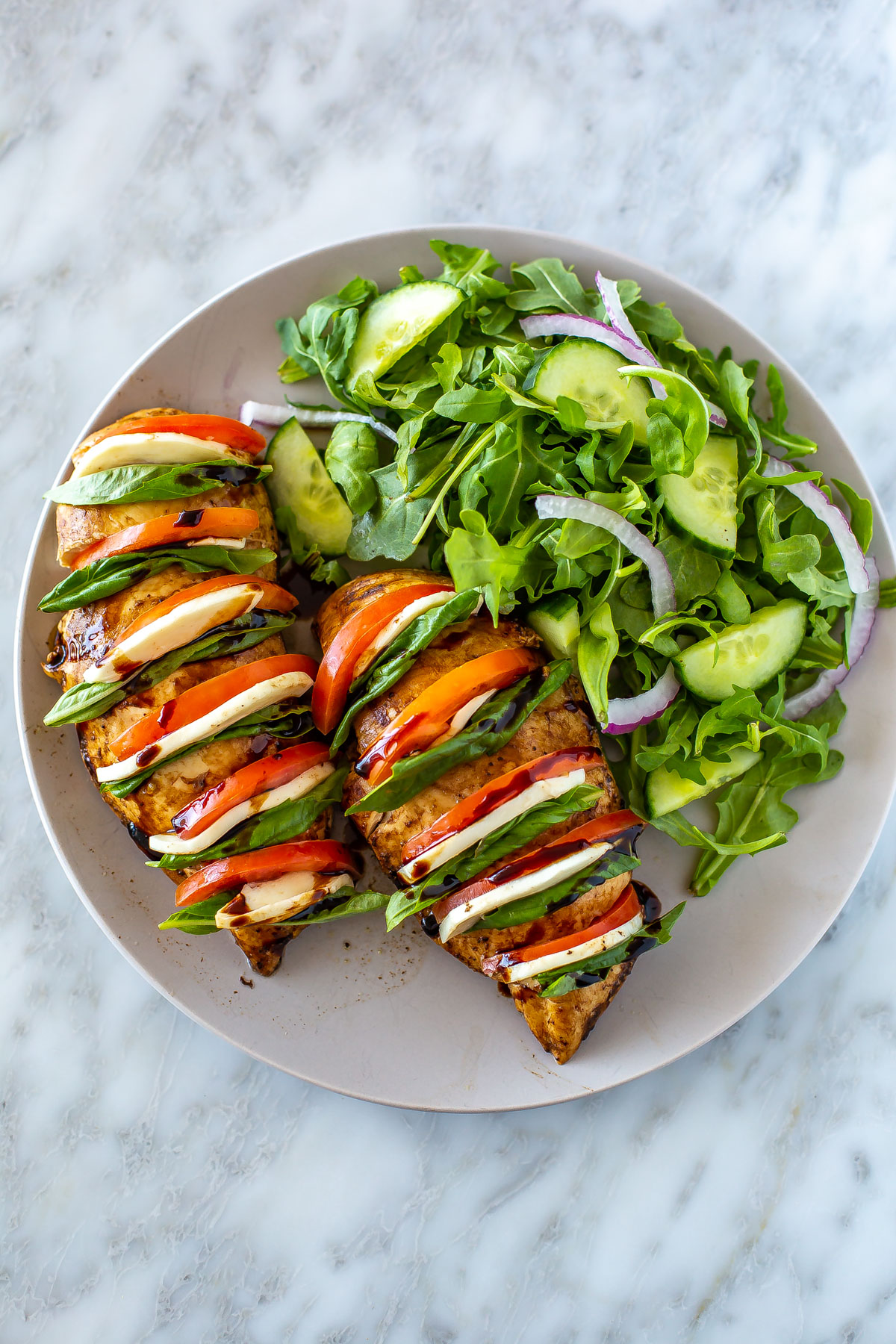 A plate with hasselback caprese chicken with a side salad.