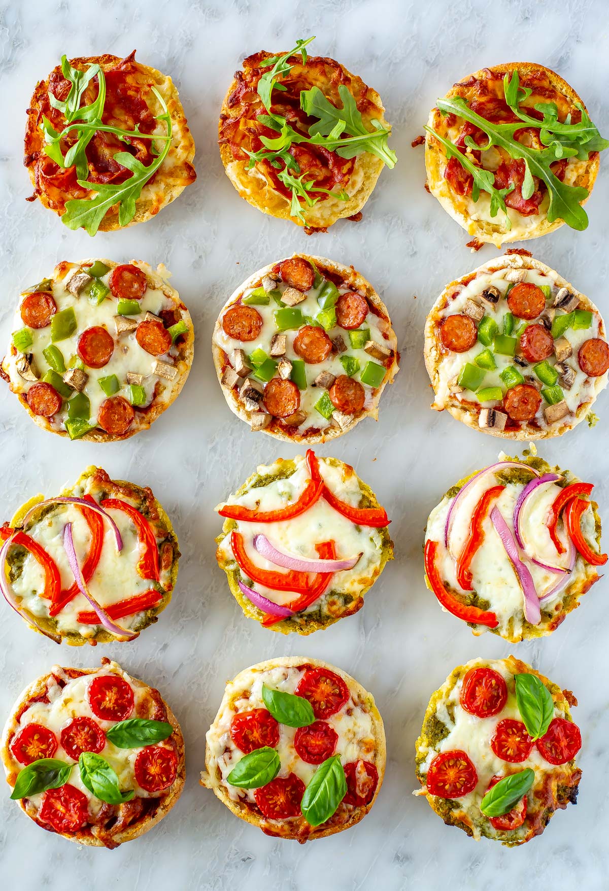 12 different english muffin pizzas on a marble slab.