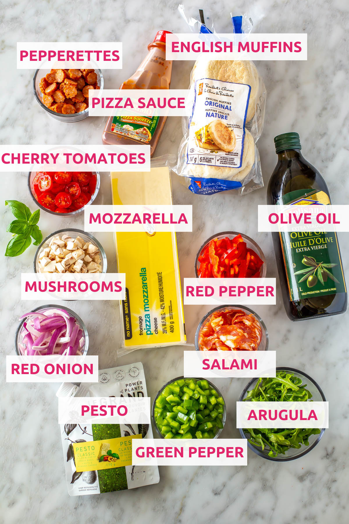 Ingredients for english muffin pizzas: english muffins, pizza sauce, mozzarella cheese, pepperettes, olive oil, cherry tomatoes, mushrooms, red pepper, red onion, salami, pesto, green pepper and arugula.