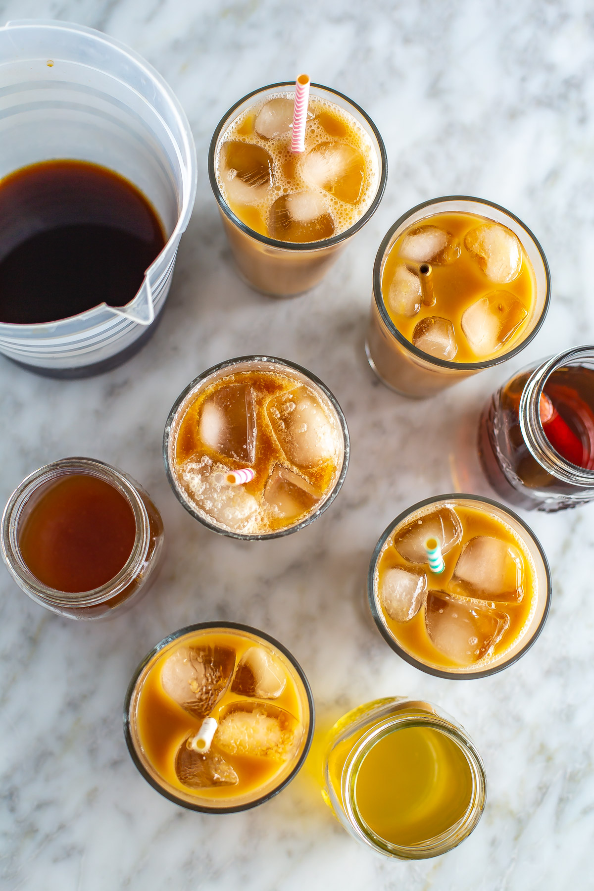 An overhead shot of 6 glasses of cold brew coffee next to a pitcher and different homemade cold brew syrups.